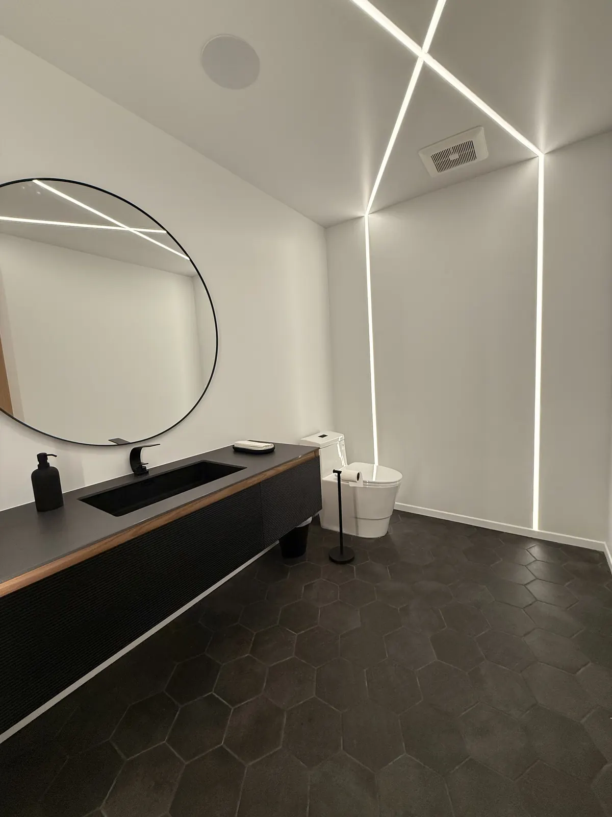 Powder room with linear lighting and a round mirror