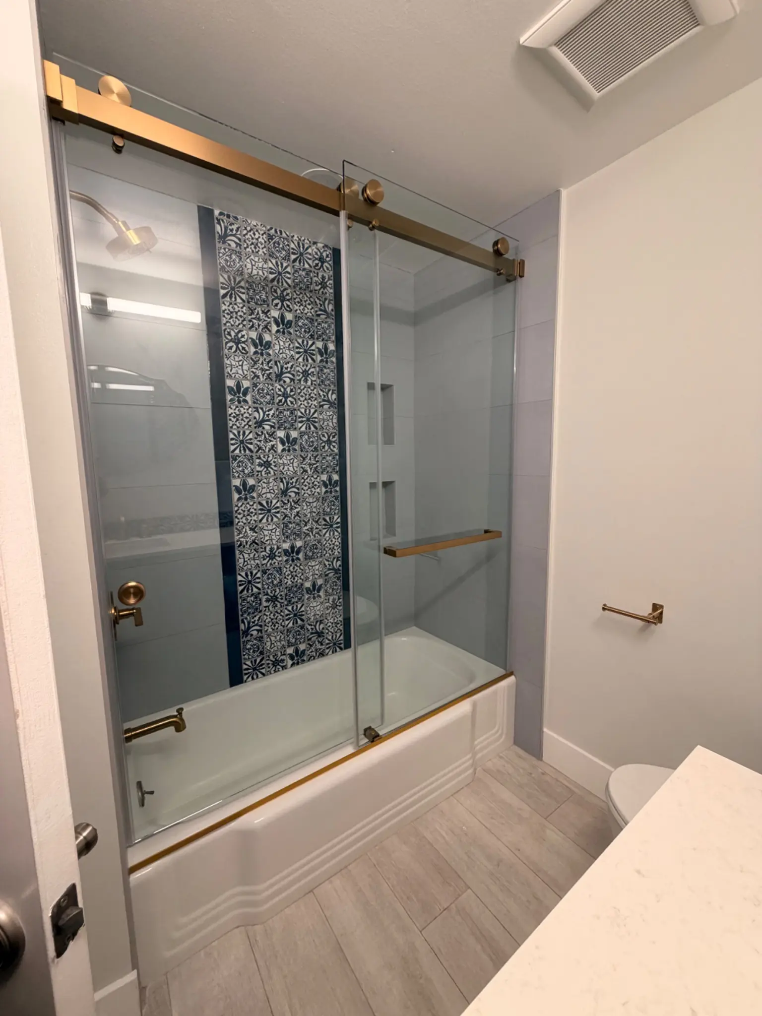 Completed Laguna Beach bathroom with patterned tile, navy cabinetry, brass-tone fixtures, and glass enclosure