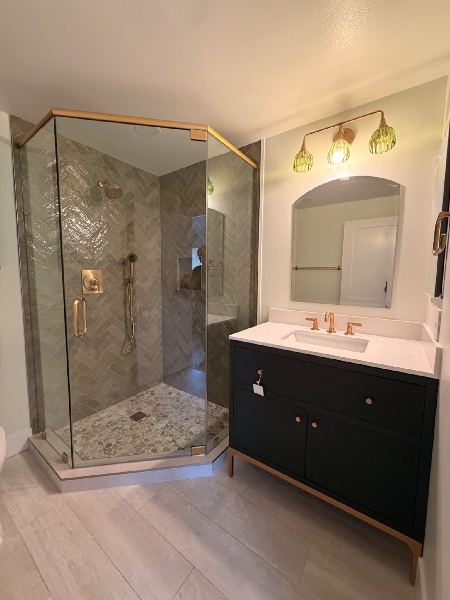 Bathroom Two after remodeling with herringbone tile, pebble floor, and frameless glass