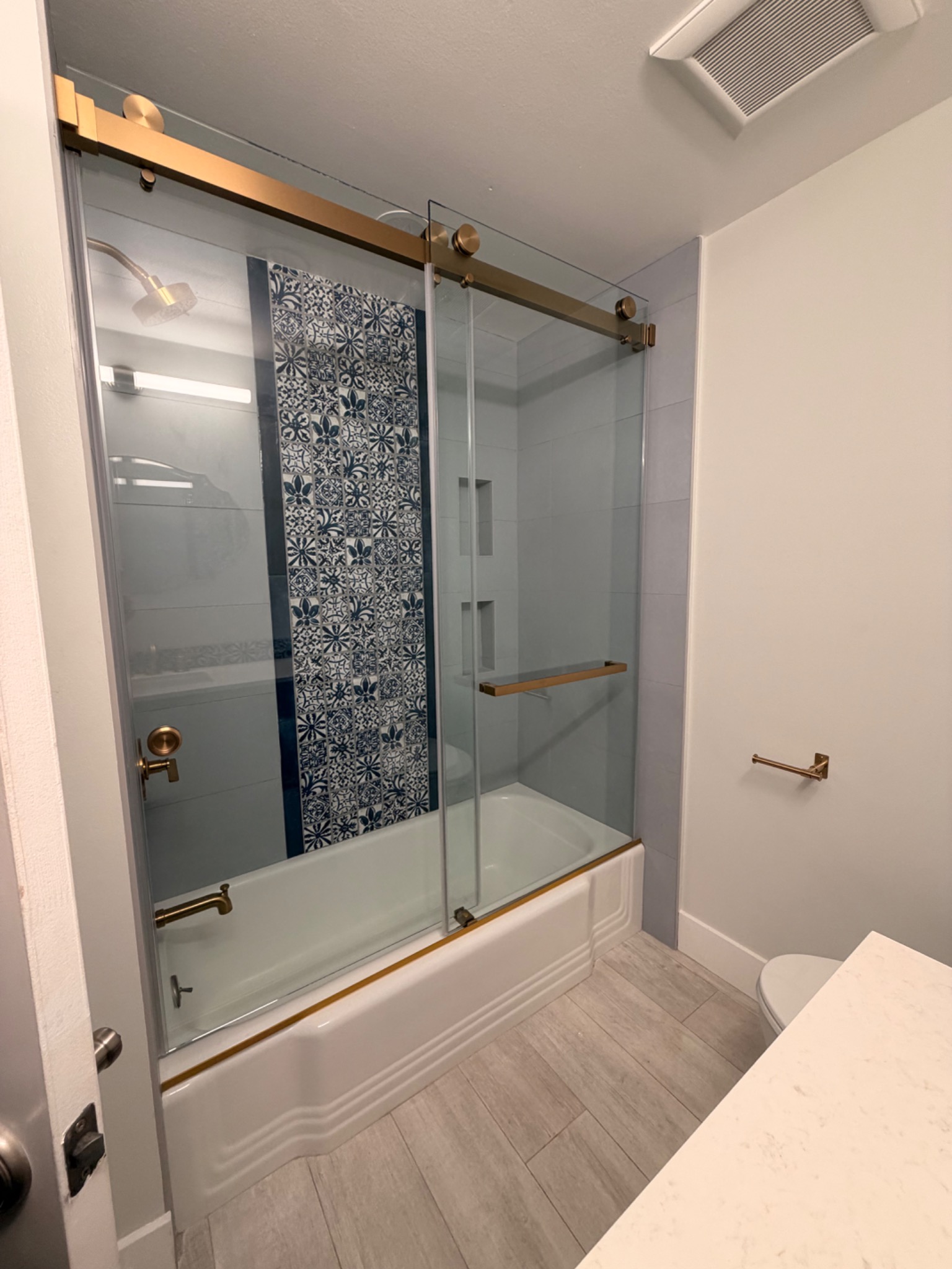Completed Laguna Niguel bathroom with patterned tile, navy cabinetry, brass-tone fixtures, and glass enclosure