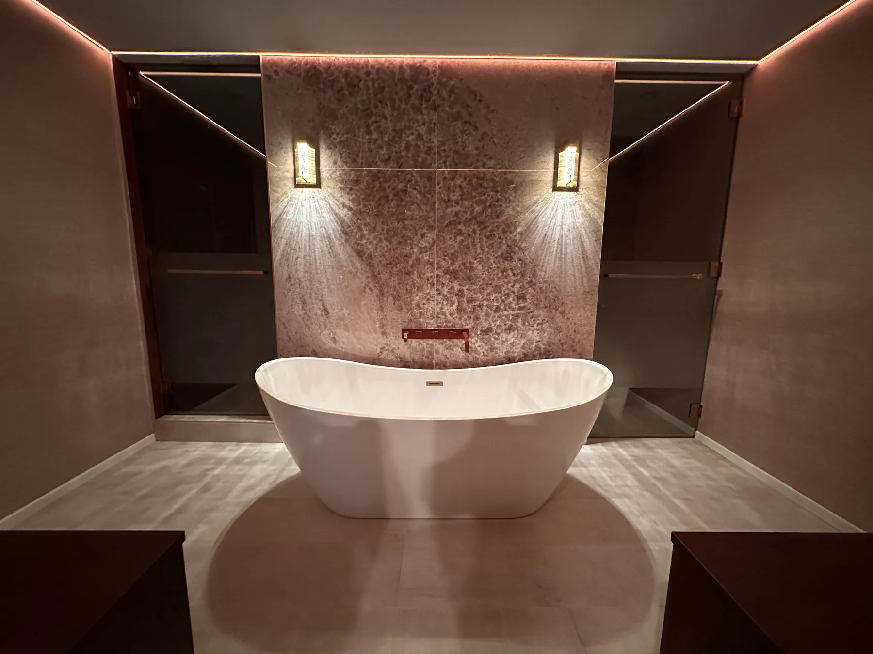 Freestanding tub in front of a backlit stone wall